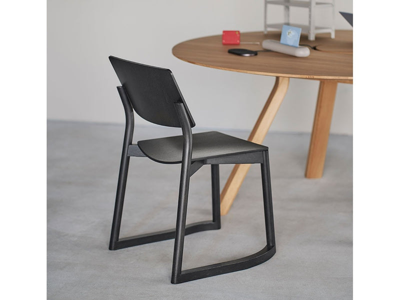 Panorama-Stuhl mit Kufen in Grain Matt Black, neben einem runden Eichentisch