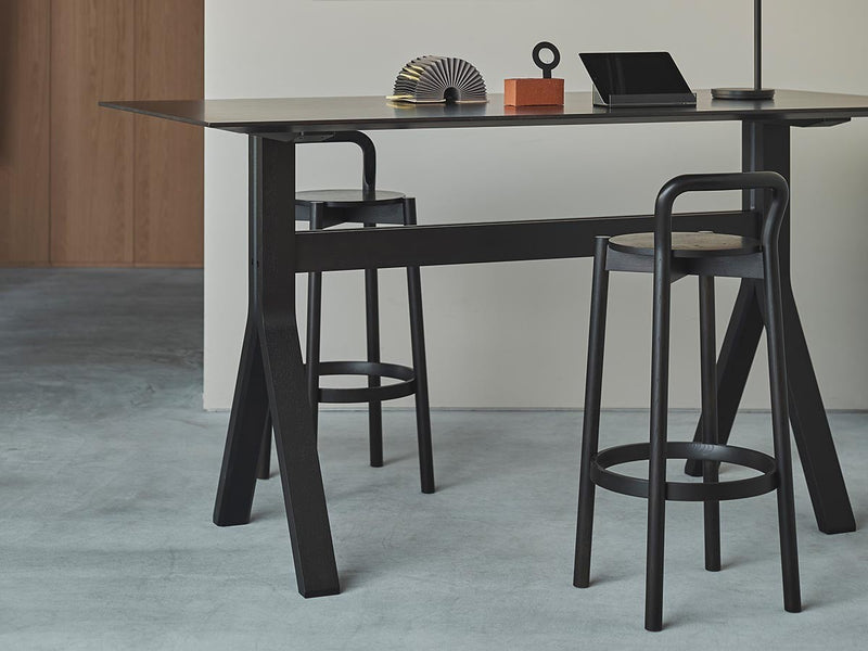 Tabourets de bar Castor à dossier noirs devant une table haute noire, dans un intérieur en béton