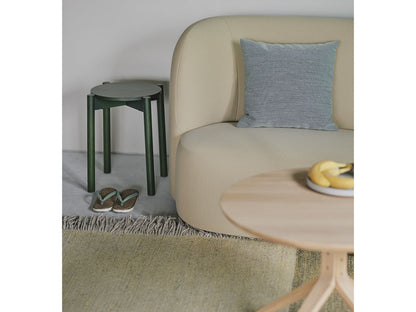 Hocker Castor Plus in Grün hinter einem beigen Sofa, mit Couchtisch aus Eiche | Antifer