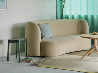 Hocker Castor Plus in Grün am Ende eines beigen Sofas, vor einem wassergrünen Vorhang | Antifer