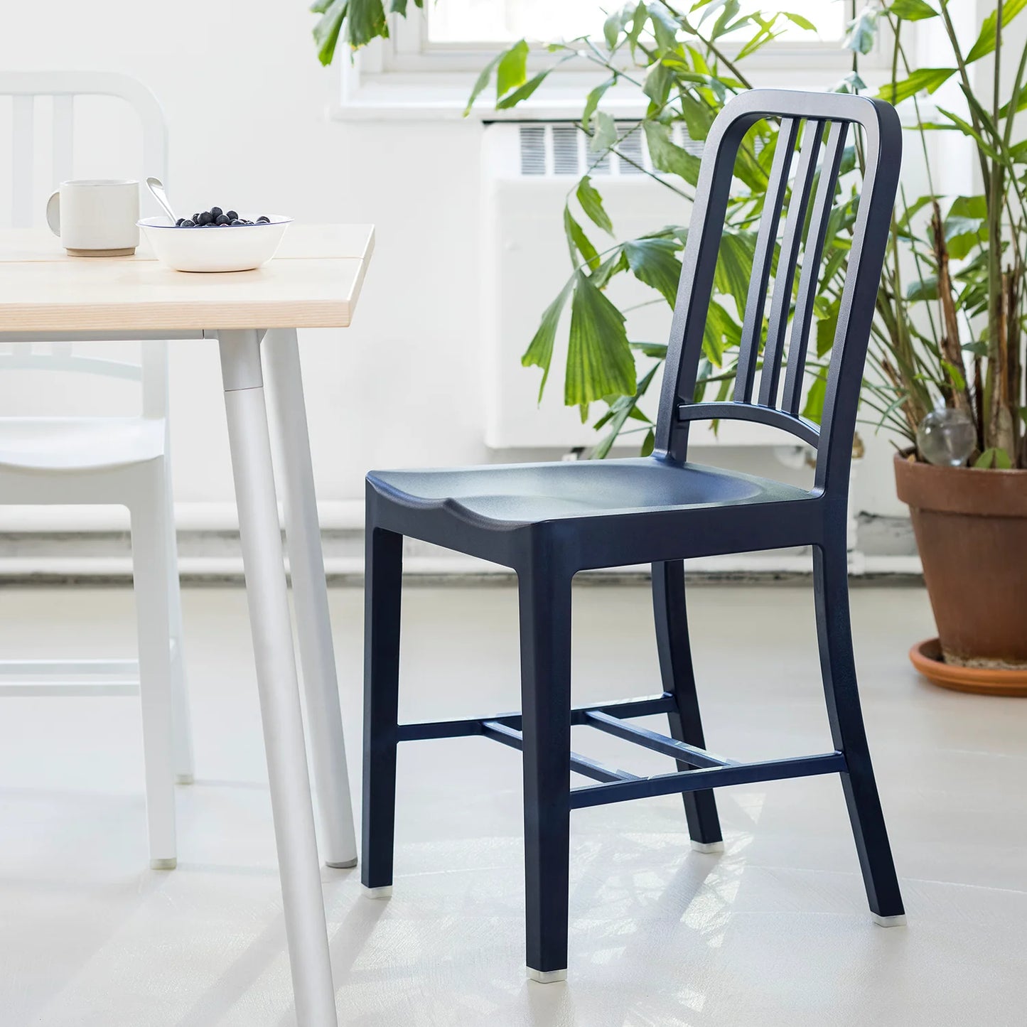 Gros plan sur une grand table avec chaise 111 Navy Emeco en plastique rPET recyclé couleur bleu marine. Café sur la table