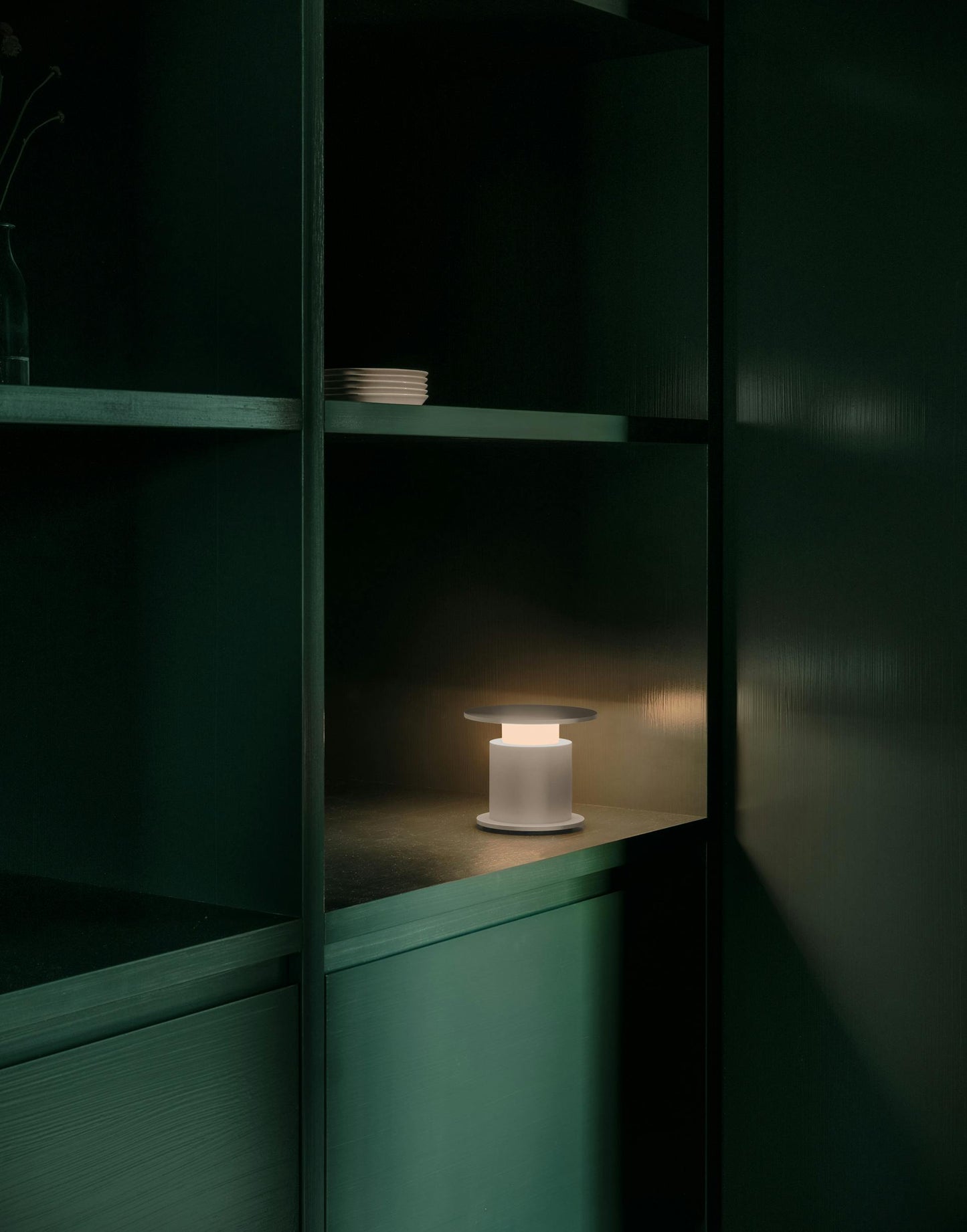 Lampe nomade w241 Faro rouge posée éclairée dans une étagère verte. Wästberg. Design David Chipperfield