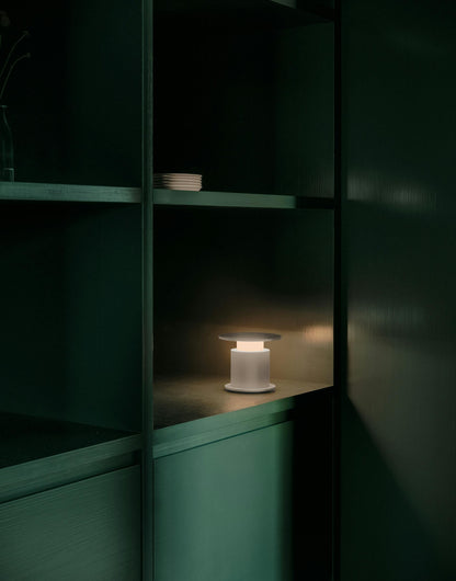 Lampe nomade w241 Faro rouge posée éclairée dans une étagère verte. Wästberg. Design David Chipperfield