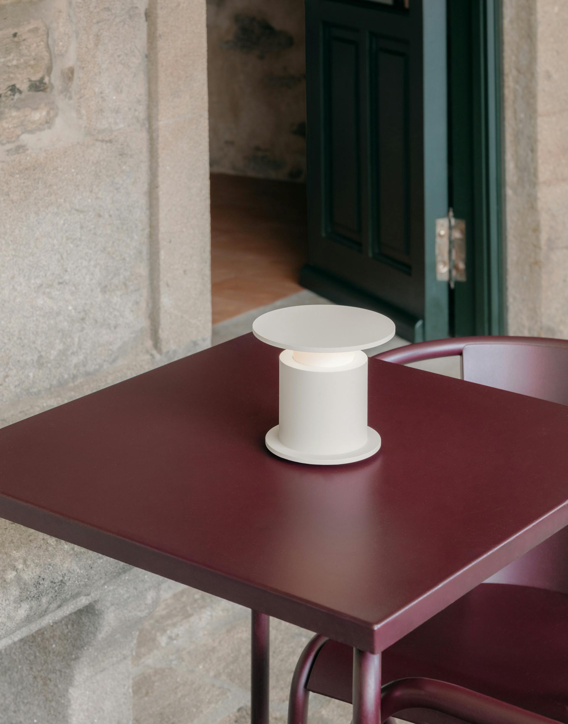 zoom sur Lampe nomade w241 Faro blanche posée sur une table bordeaux. Wästberg. Design David Chipperfield