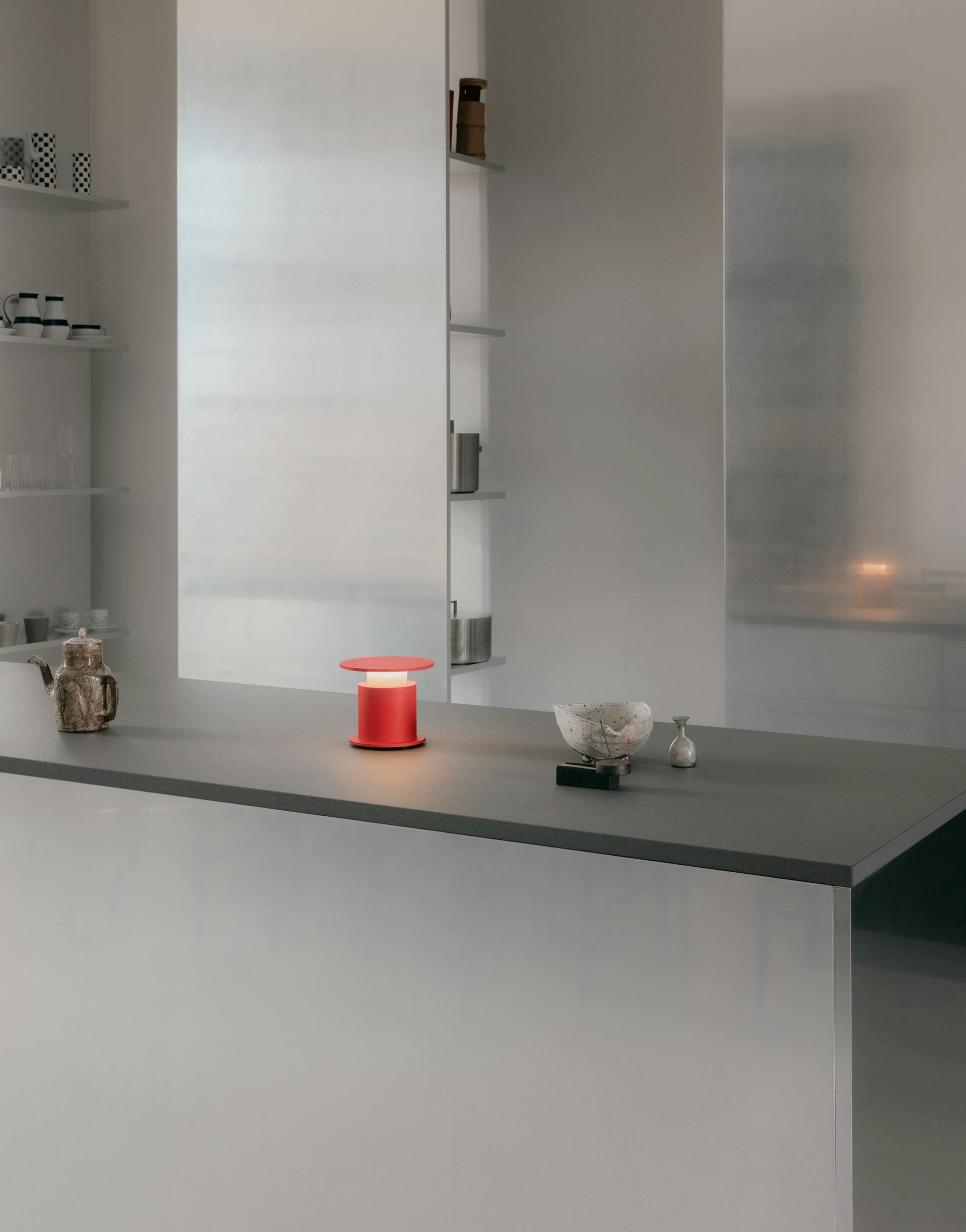 Lampe nomade w241 Faro rouge posée sur un plan de travail. Wästberg. Design David Chipperfield