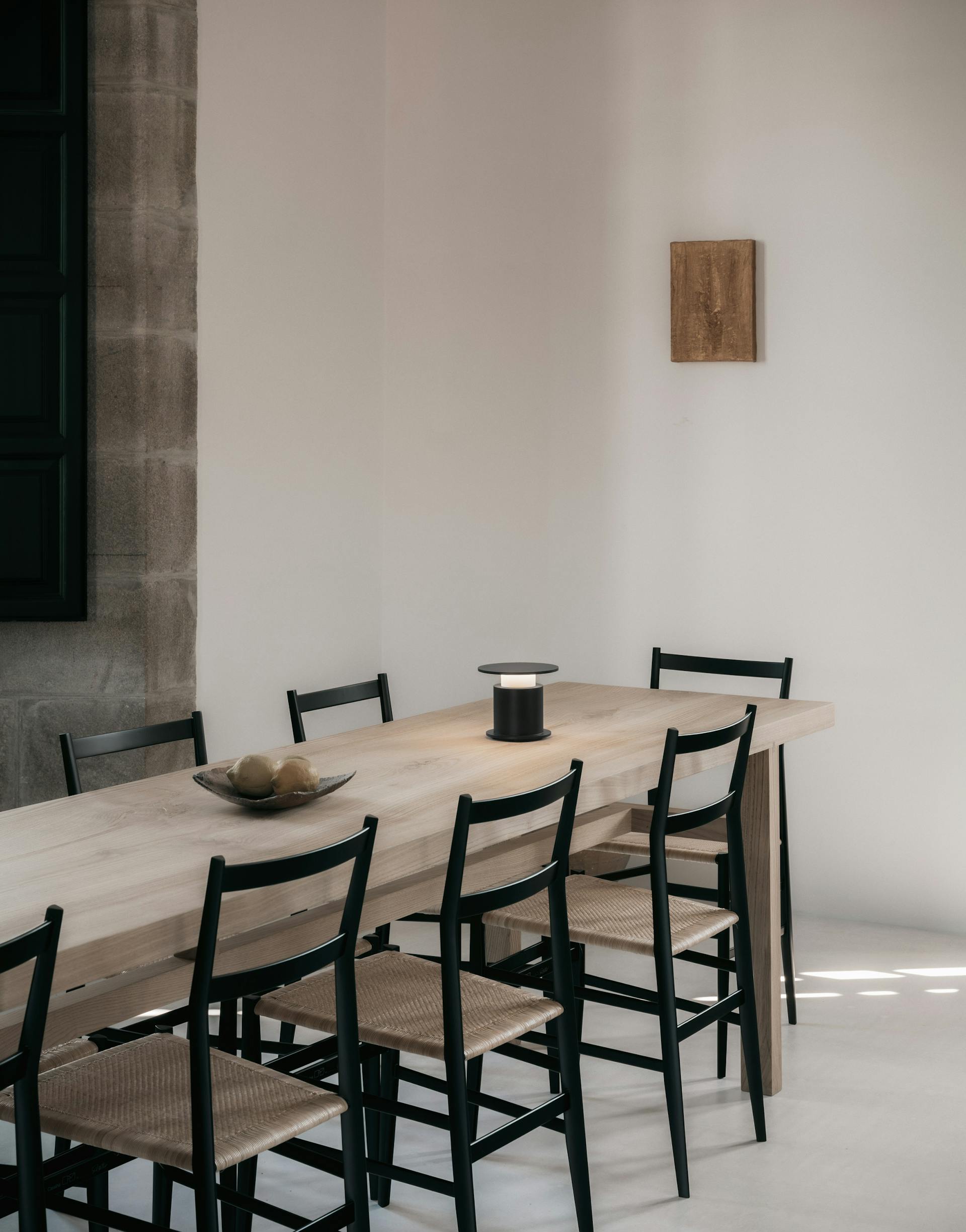 Lampe nomade w241 Faro noire posée sur une grande table communale avec 8 chaises. Wästberg. Design David Chipperfield