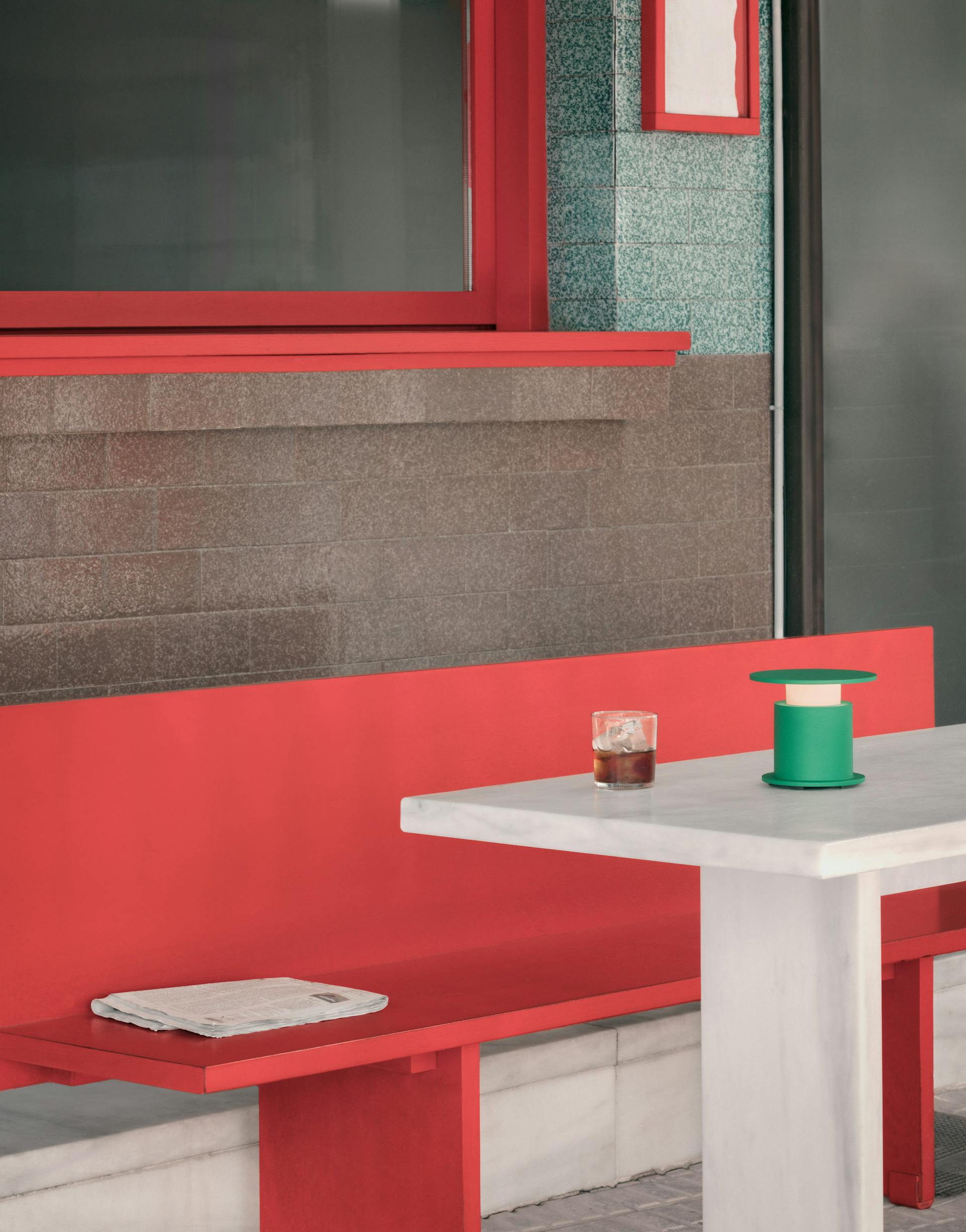 Lampe nomade w241 Faro verte posée sur une table blanche, banc rouge. Wästberg. Design David Chipperfield