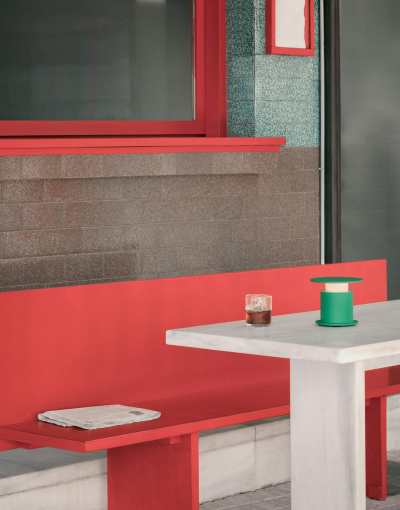 Lampe nomade w241 Faro verte posée sur une table blanche, banc rouge. Wästberg. Design David Chipperfield