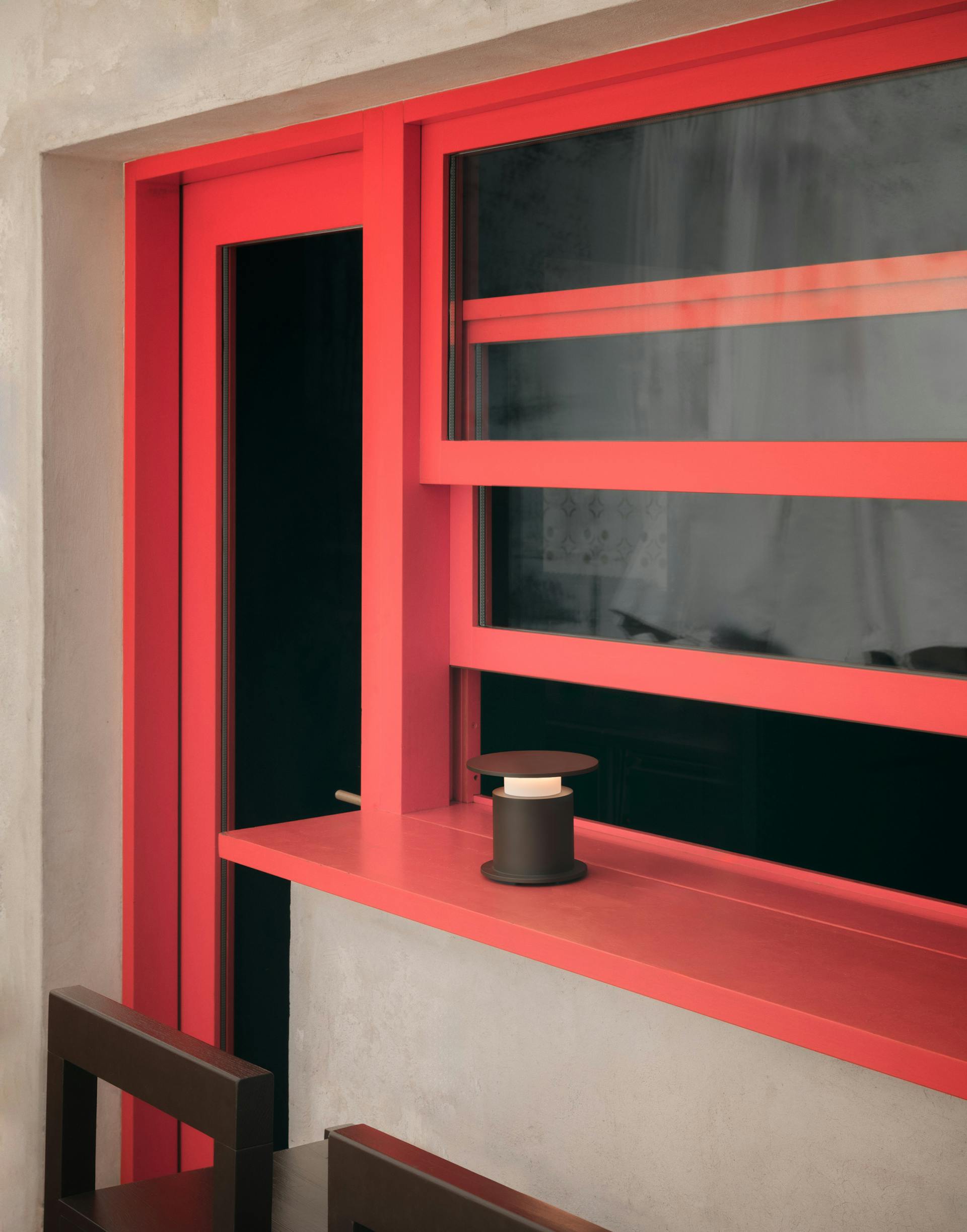 Lampe nomade w241 Faro chocolat posée sur un passe plat rouge. Wästberg. Design David Chipperfield