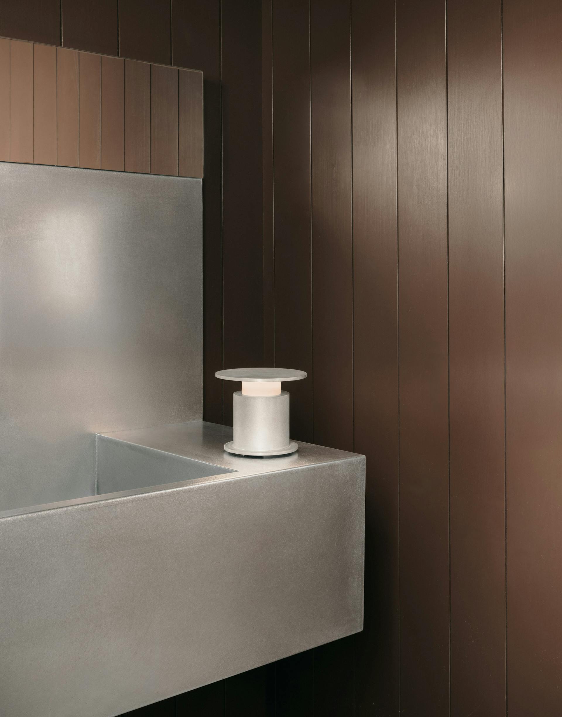 Lampe nomade w241 Faro aluminum brut posée sur un coin de salle de bain. Wästberg. Design David Chipperfield