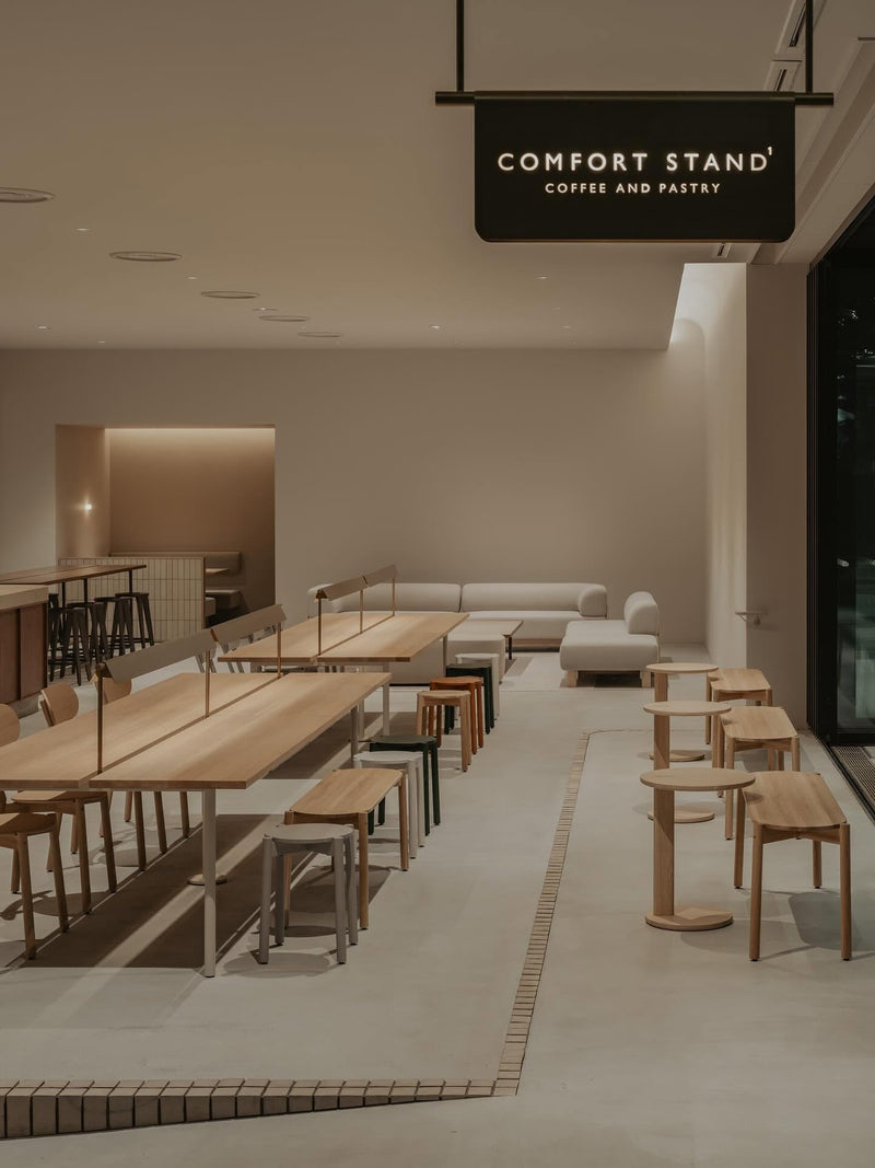 Cafetería con largas mesas de roble, bancos y taburetes Castor, sofás modulares al fondo
