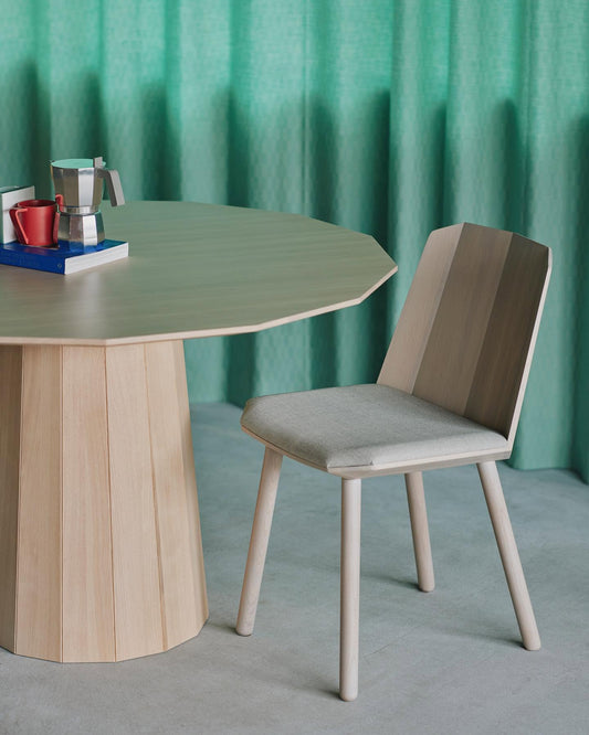 Chaise Colour Wood en châtaignier devant une table Colour Wood, sur fond de rideau vert | Antifer